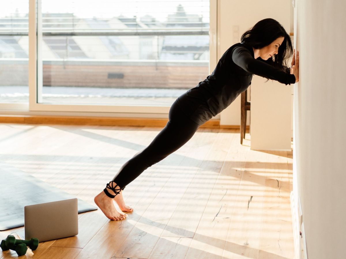 Wand Pilates Übungen: Frau in schwarzer Trainingskleidung macht Wall Push up