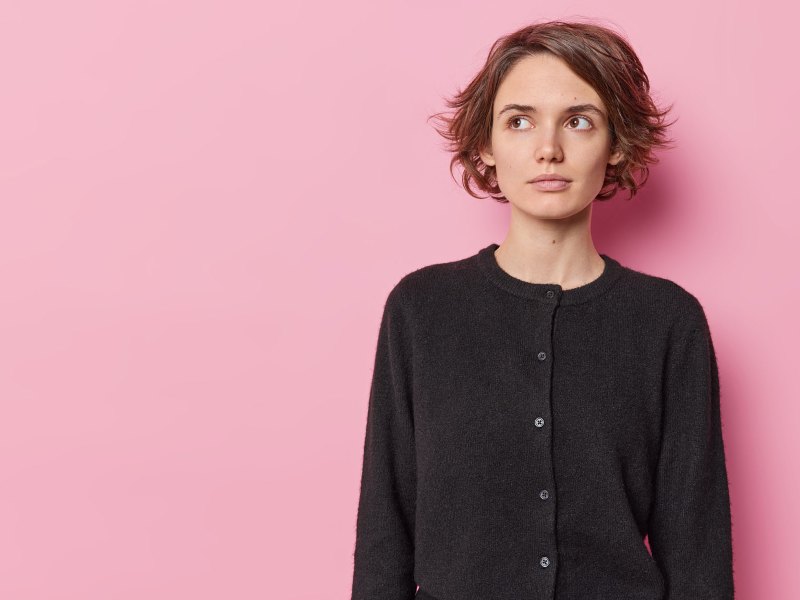 Frau vor einer pinken Wand blickt ernst zur Seite