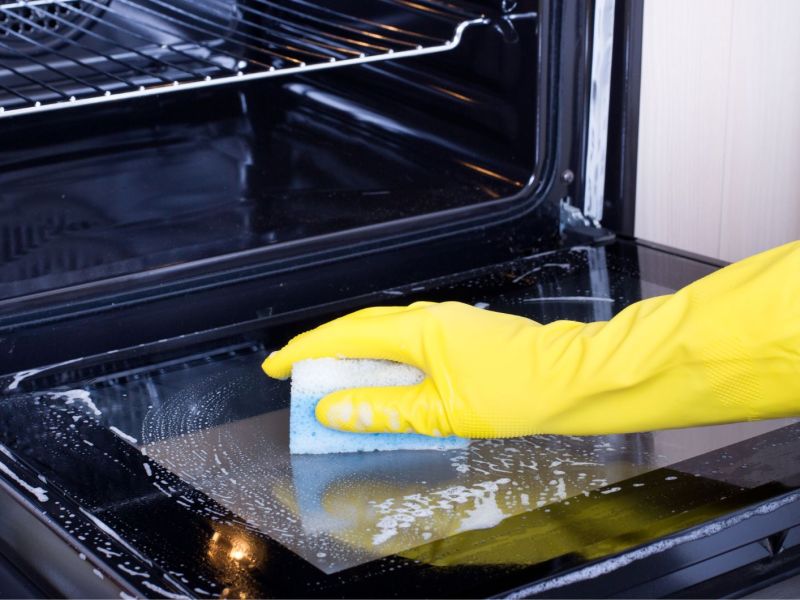 Person reinigt Backofen mit einem Schwamm