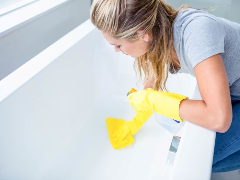 Eine Frau putzt mit Schwamm und Reiniger die Badewanne