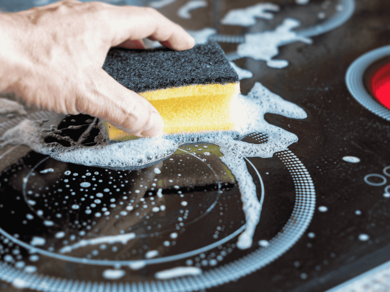 Person reinigt Ceranfeld mit einem Schwamm