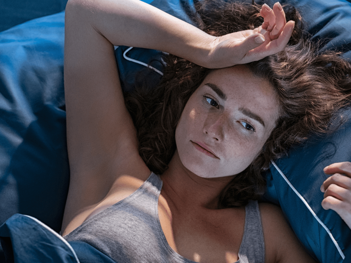 Frau im Bett, die sich nachdenklich und erschöpft auf die Stirn packt.