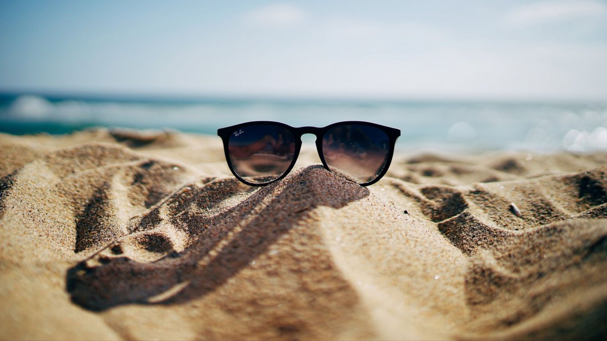 Sonnenbrille, die im Sand liegt mit Strand und Meer im Hintergrund.