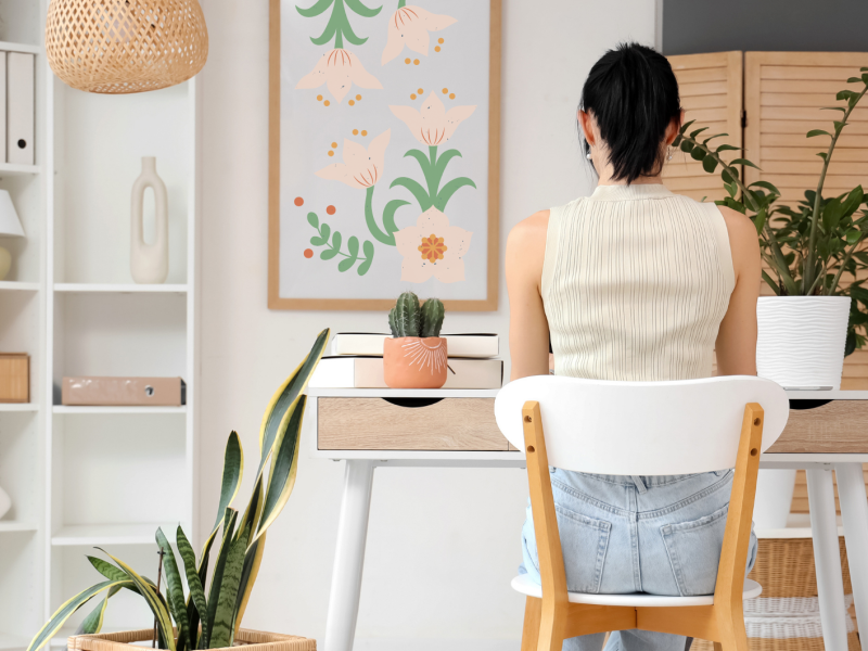 Junge Frau arbeitet am Schreibtisch in einem hellen Heimbüro, Rückenansicht