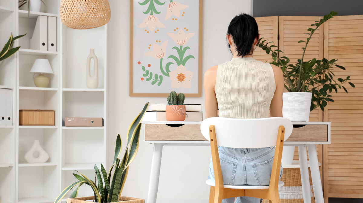 Junge Frau arbeitet am Schreibtisch in einem hellen Heimbüro, Rückenansicht