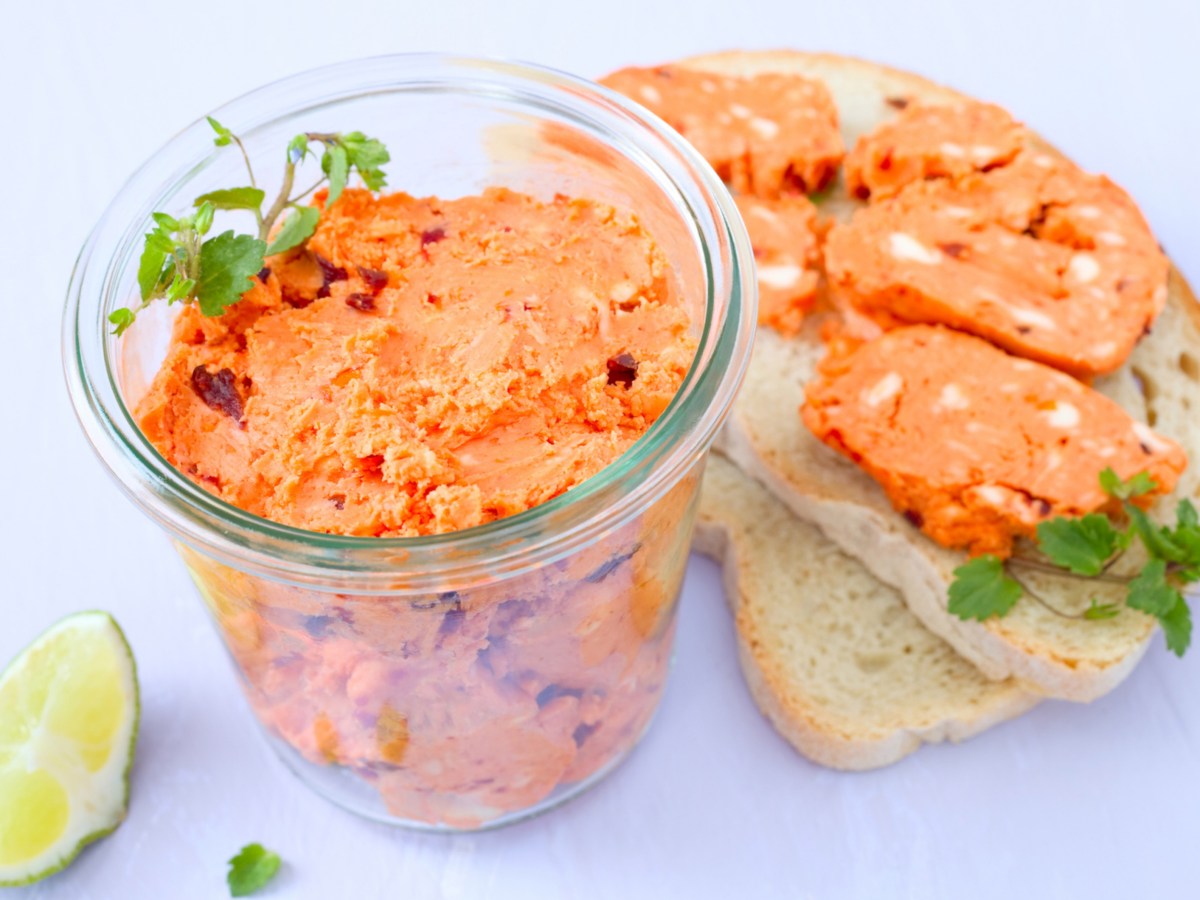 Tomatenbutter in einem Glasgef&auml;&szlig;, daneben zwei Scheiben Brot mit Tomatenbutter.