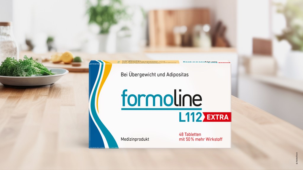 Eine Packung Formoline L112 EXTRA für Übergewicht auf einem Holztisch in einer hellen Küche, daneben frische Kräuter.