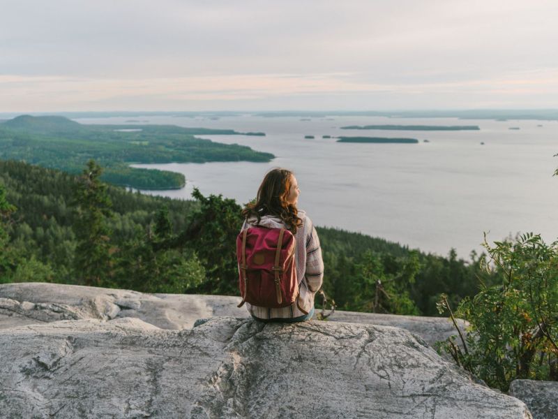 Eine Frau mit Rucksatz sitzt auf einer Klippe und schaut zum Horizont