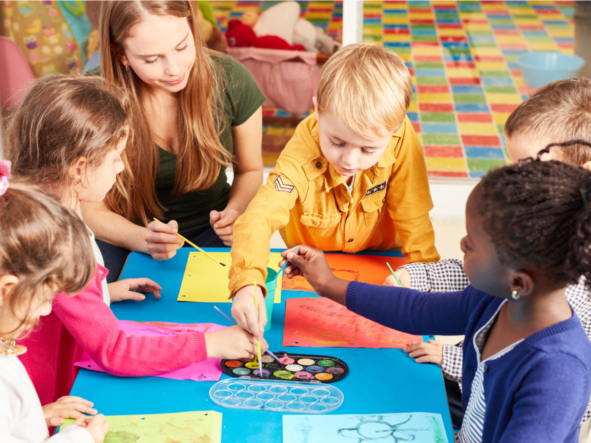 Kleinkinder sitzen an einem kleinen Tisch und malen mit ihrer Erzieherin