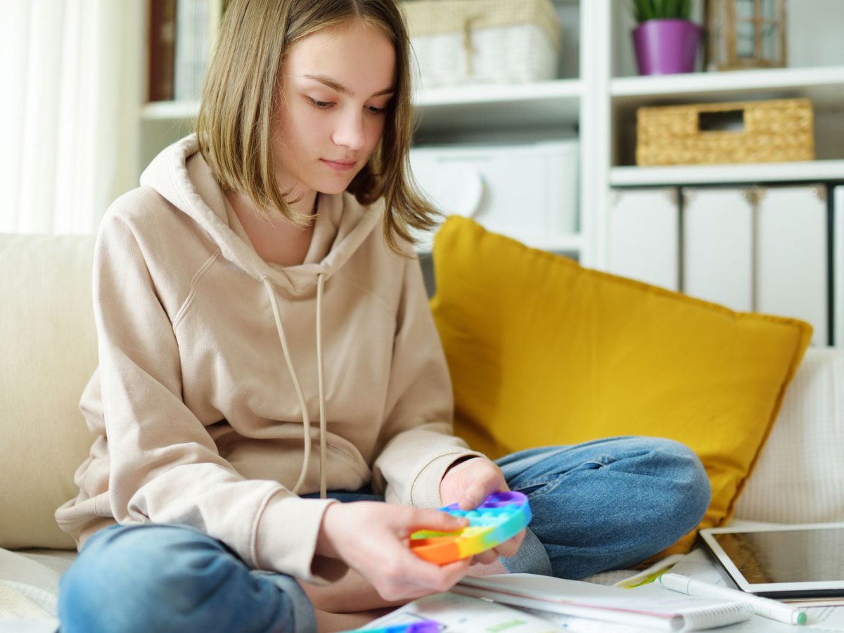 Teenagerin, ca. 14 Jahre, sitzt auf dem Bett, ist umgeben von Unterlagen und dr&uuml;ckt zur Entspannung auf einem Pop-it herum.