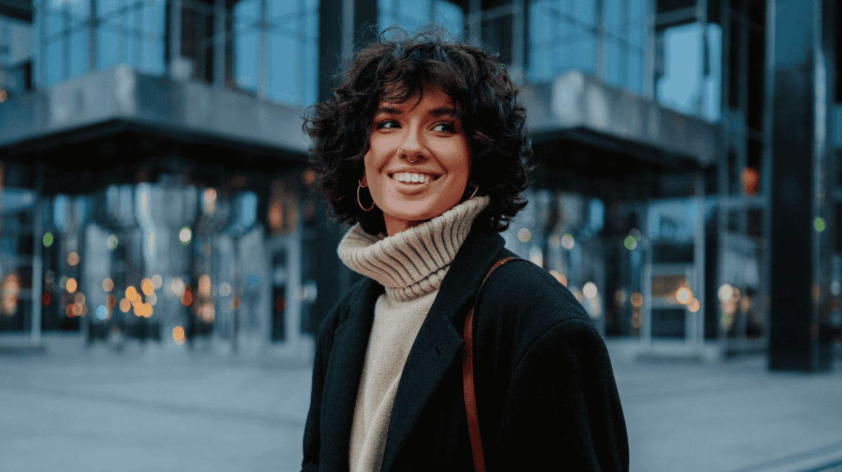 Junge Frau mit Pullover und Mantel lächelt in Kamera.