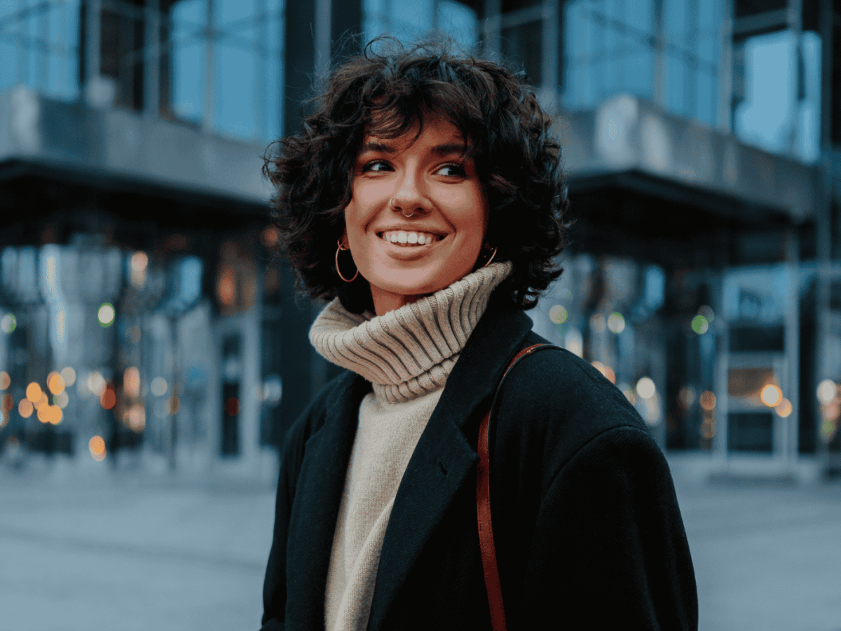 Junge Frau mit Pullover und Mantel lächelt in Kamera.