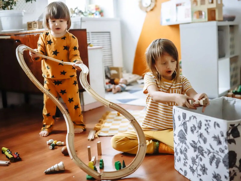Zwei Kinder in ihrem Kinderzimmer beim Aufr&auml;umen der Spielsachen.