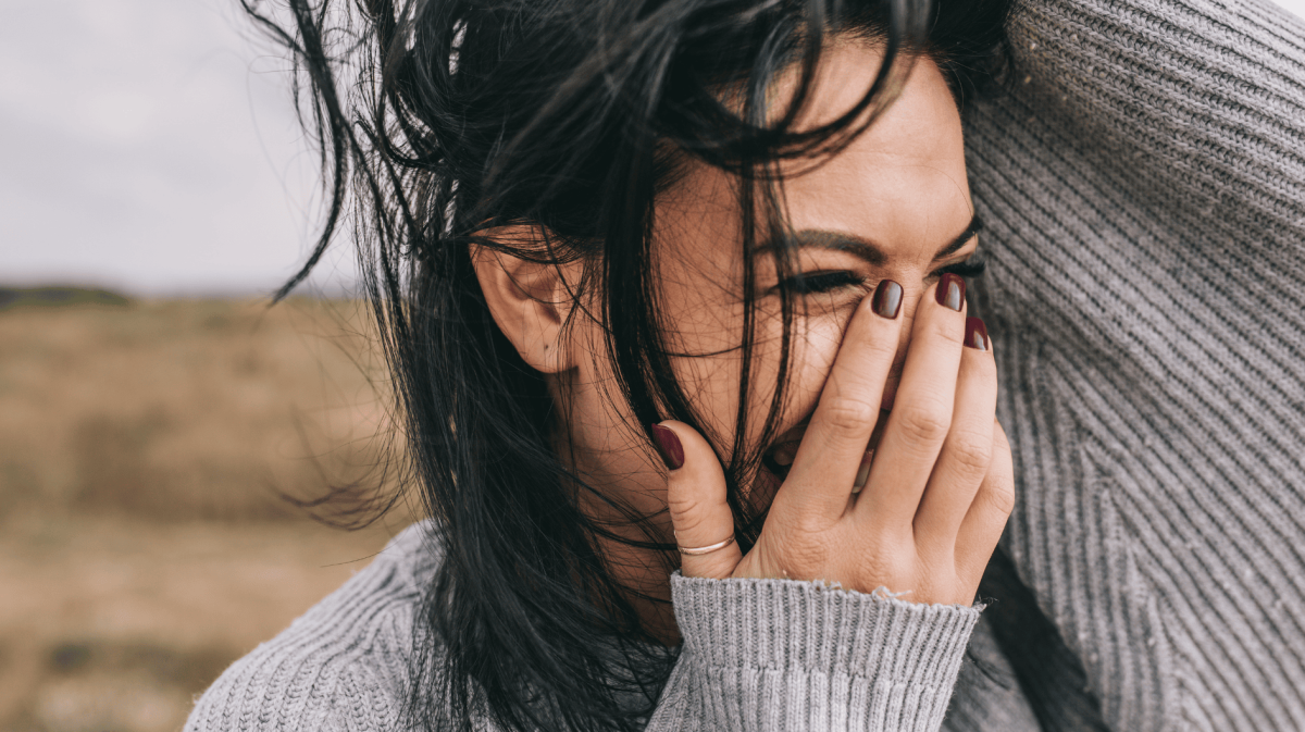 Frau mit dunklen Haaren hält sich lachen Hand vor Mund.