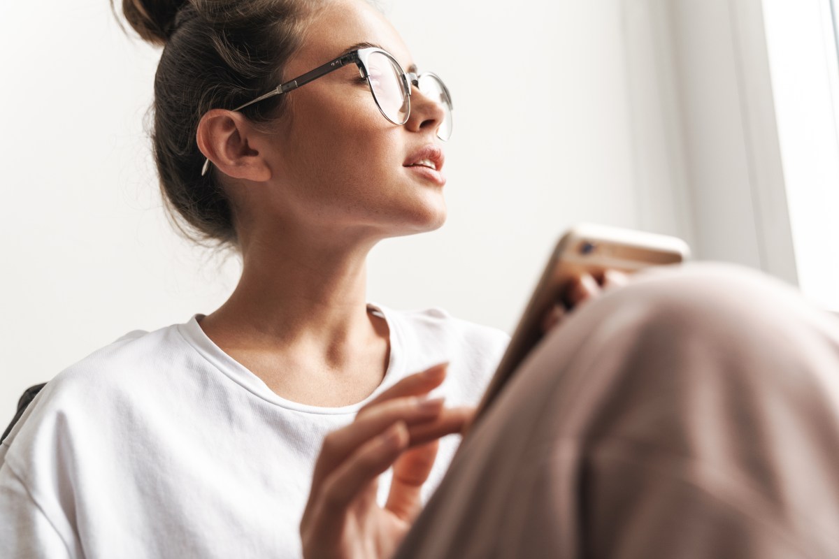 Frau mit Brille sitzt auf dem Sofa mit einer Decke über den Beinen und schaut aus dem Fenster