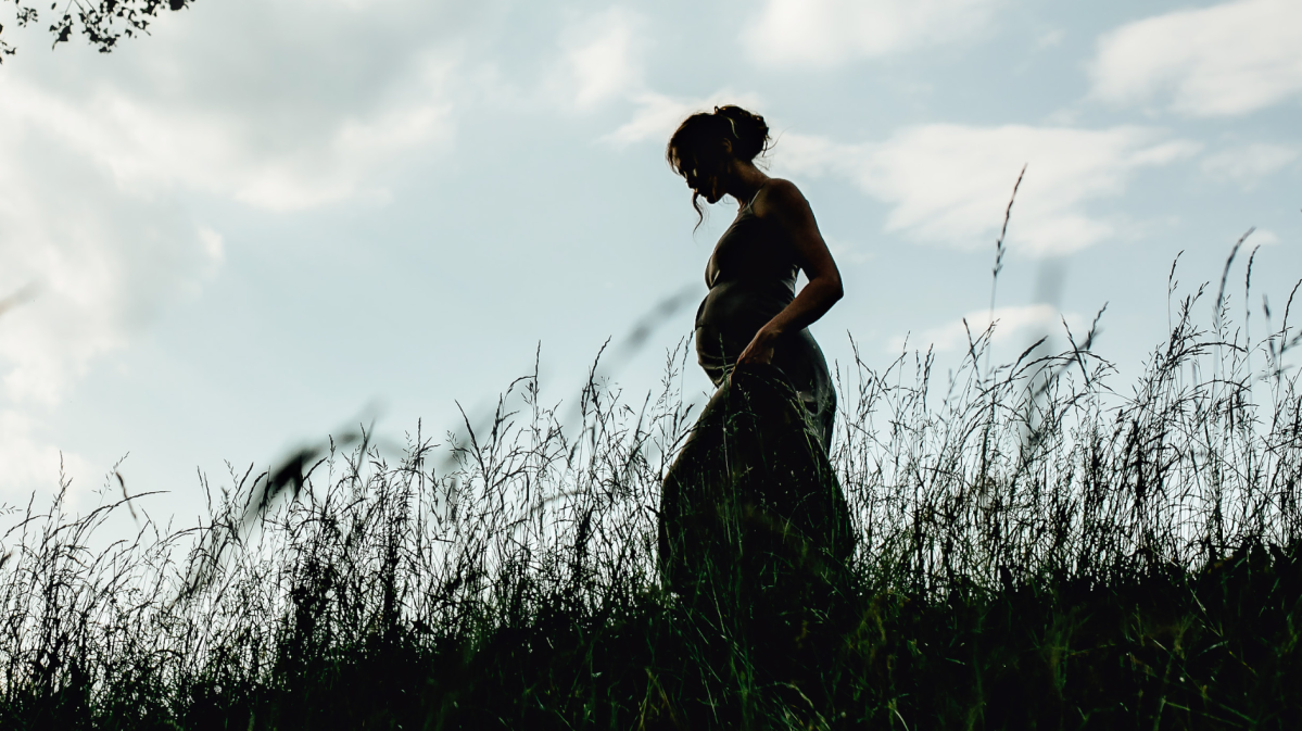 schwangere Frau vor einem Sonnenuntergang über dem Meer