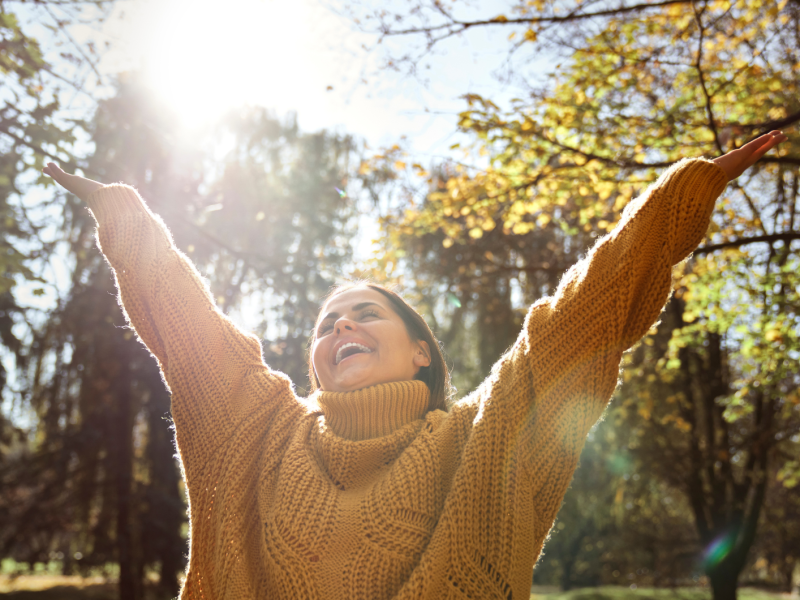 Frau im Wald, die glücklich ihre Hände in die Luft wirft und lacht.