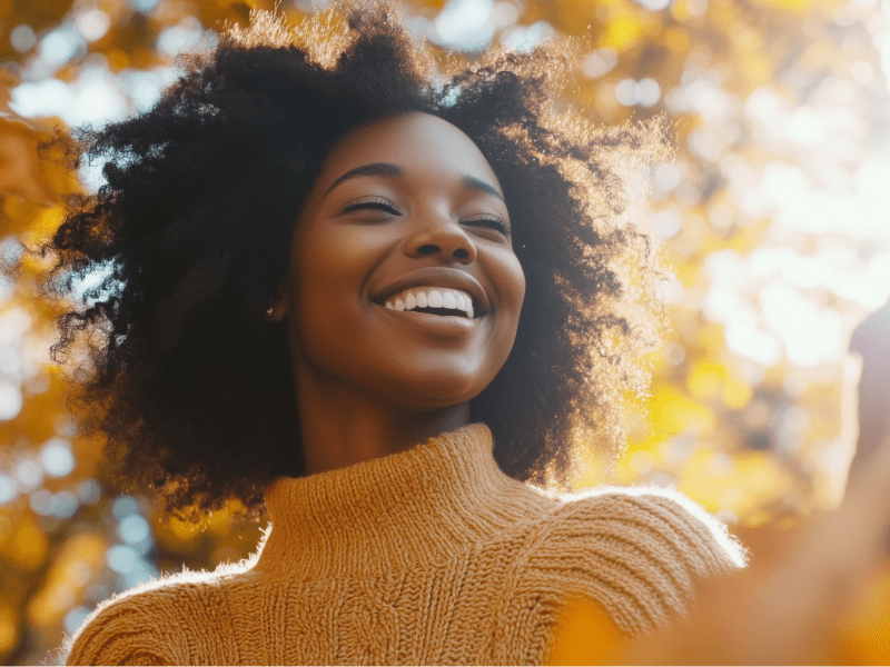 KI-generierte Frau, die lächelt, während im Hintergrund ein Laubbaum zu sehen ist.