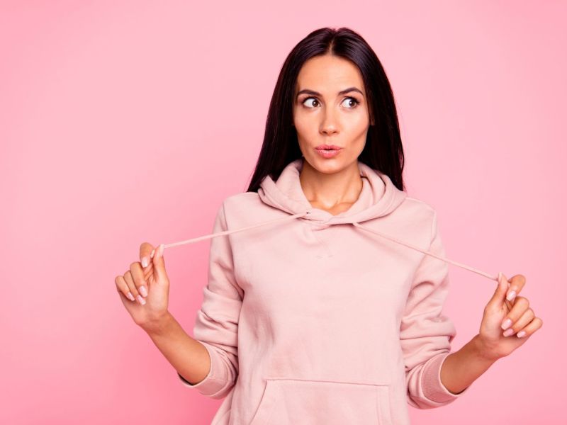 Frau mit braunen Haaren vor rosa Hintergrund mit rosa Hoodie an