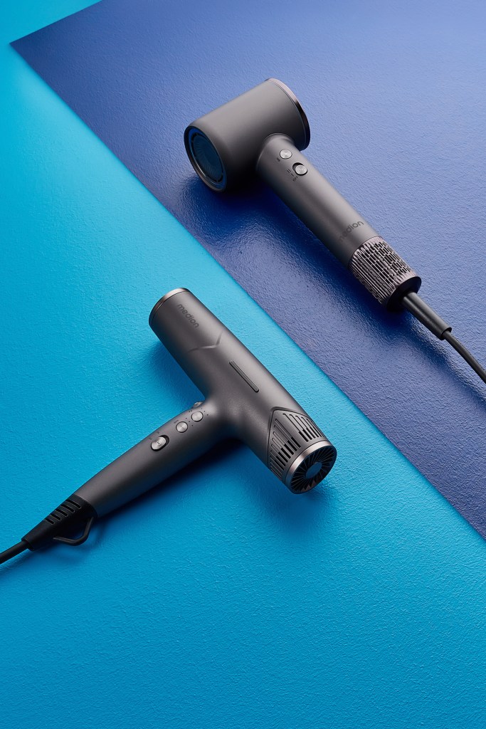 Zwei schwarze Haartrockner in modernem Design liegen auf einem blau schattierten Untergrund, leicht schräg zueinander ausgerichtet.