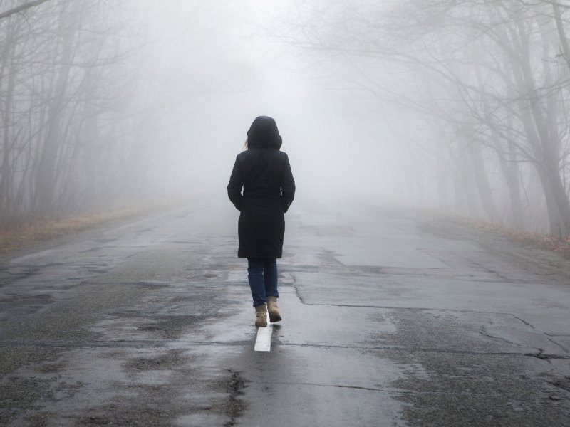 Frau mit Kapuze auf langer dunkler Stra&szlig;e