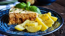 Ein blauer Teller, auf dem ein Stück ungarisches Schichtkraut liegt, angerichtet mit ein paar Kartoffelstücken.