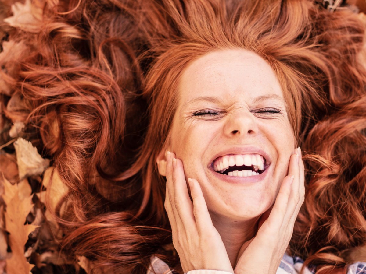 Frau mit roten Haaren liegt l&auml;chelnd im Herbstlaub