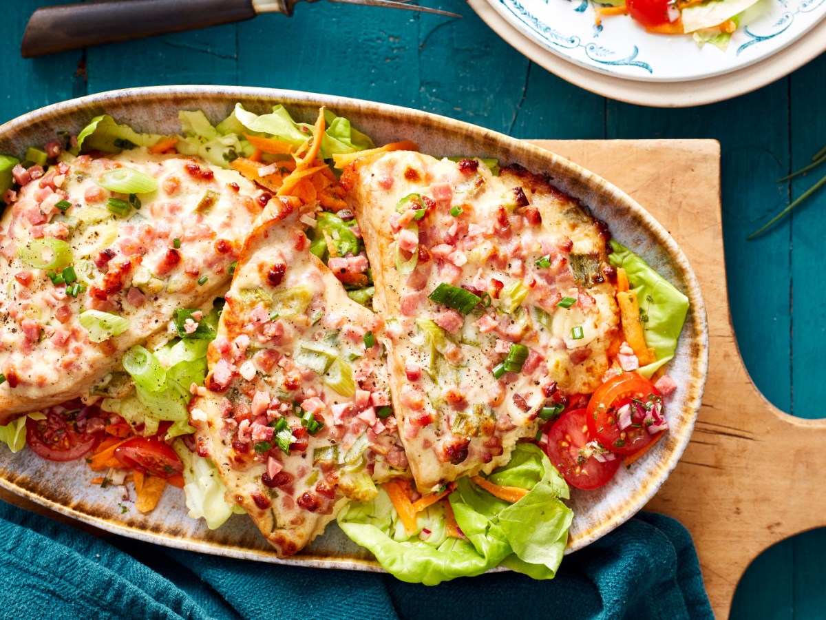 Schnitzel &uuml;berbacken mit Flammkuchen Topping auf Salatbett.