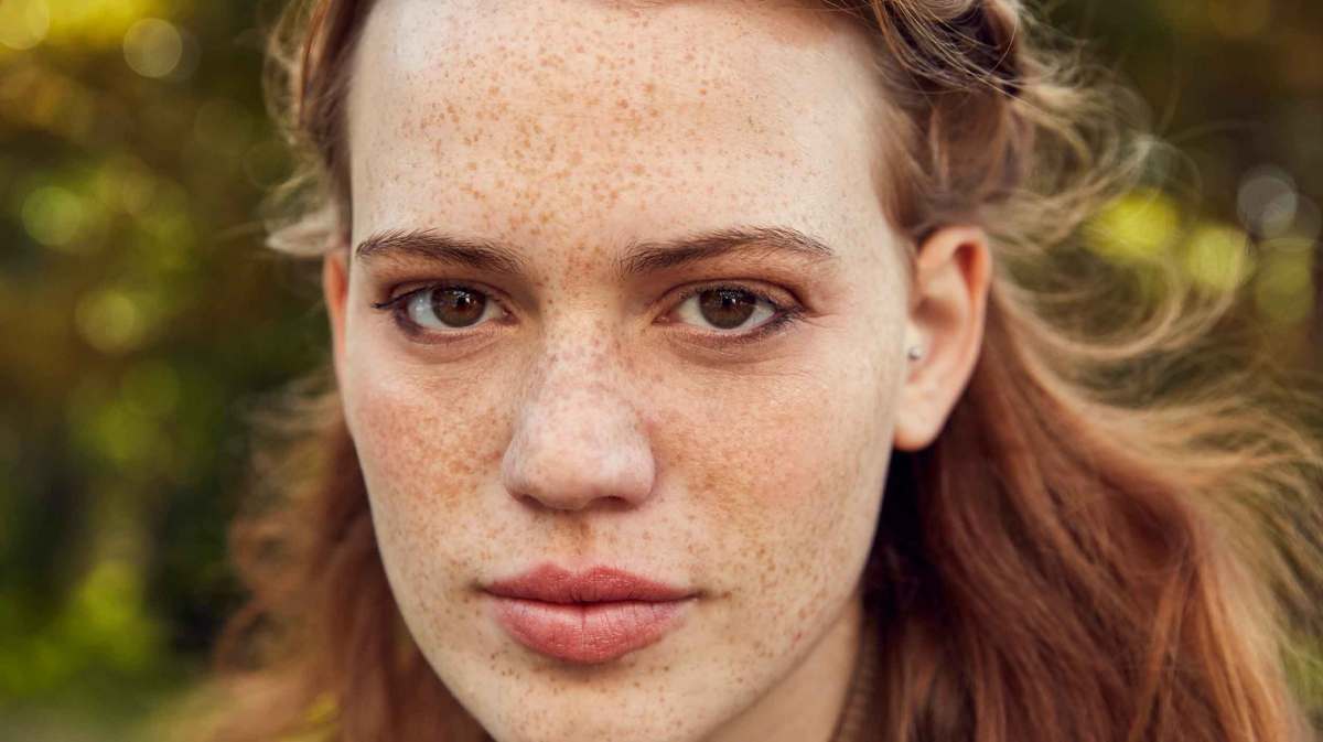 Nahaufnahme einer Frau mit Sommersprossen und rötlichen Haaren und braunen Augen.