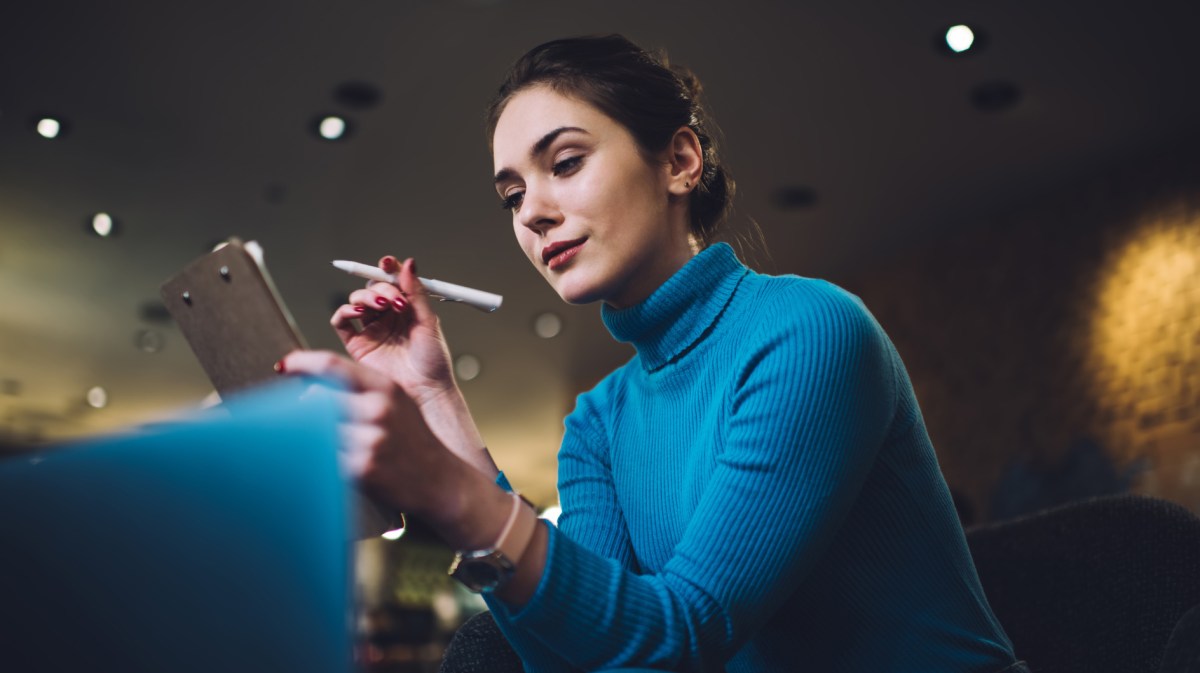 Frau in blauem Pullover schaut nachdenklich auf ihr Tablet.