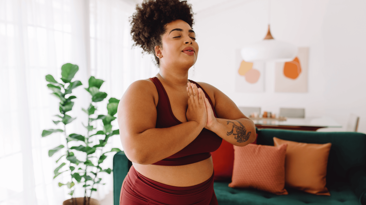 Frau vor Couch, die Yoga macht und die Hände vor der Brust zusammenlegt