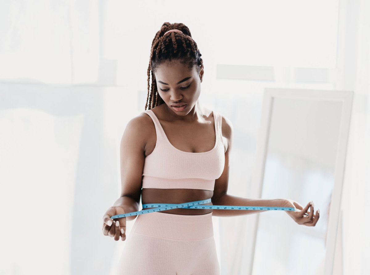 Unzufriedene junge Frau, die ihre Taille mit einem Maßband misst und sich über die Ergebnisse einer Schlankheitsdiät ärgert, weil sie nicht abnimmt