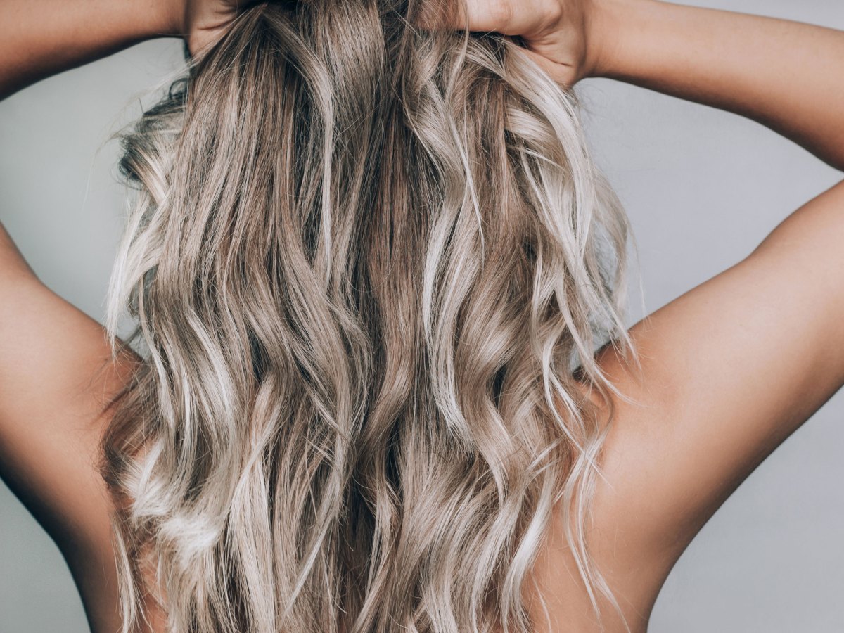 Frau fährt sich mit den Händen durch ihre langen blonden Haare.