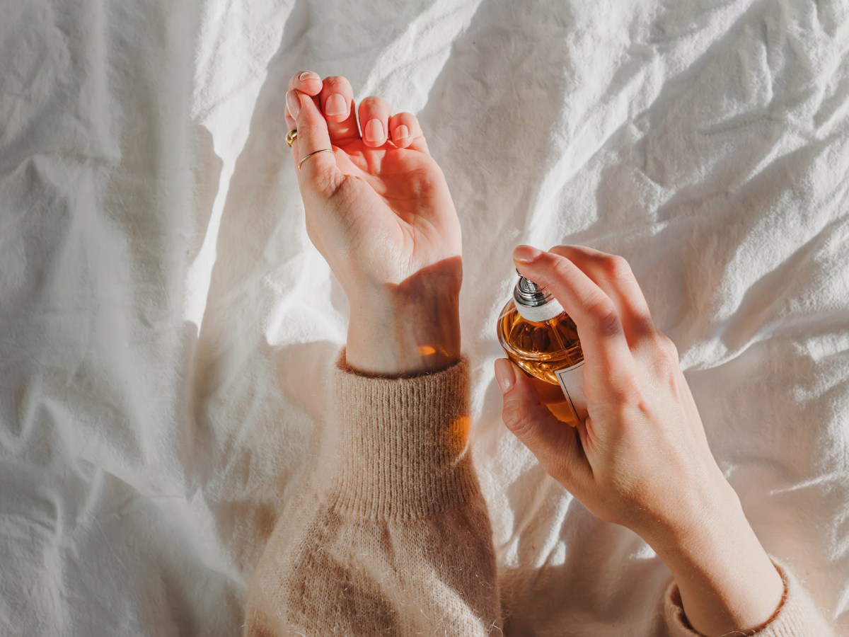 Frauenhände, die Parfum auf Handgelenk aufspürhen