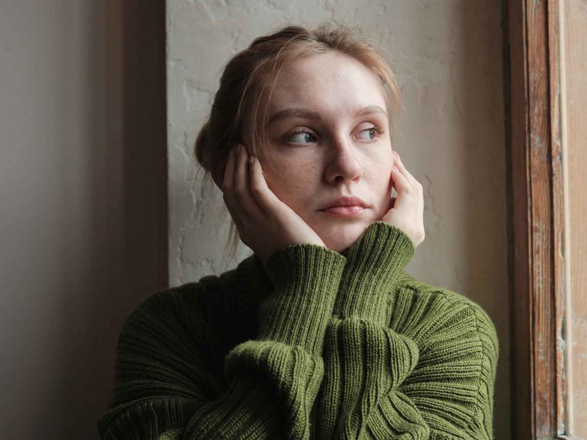 Junge Frau mit grünem Pullover guckt nachdenklich nach draußen.