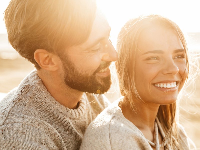 Frau und Mann nebeneinander, frau lächelt in die Kamera, Mann lächelt Frau an