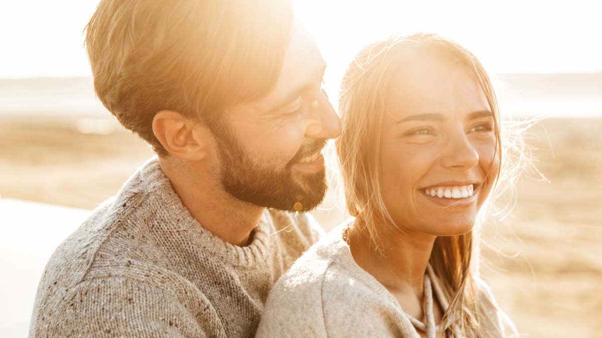 Frau und Mann nebeneinander, frau lächelt in die Kamera, Mann lächelt Frau an