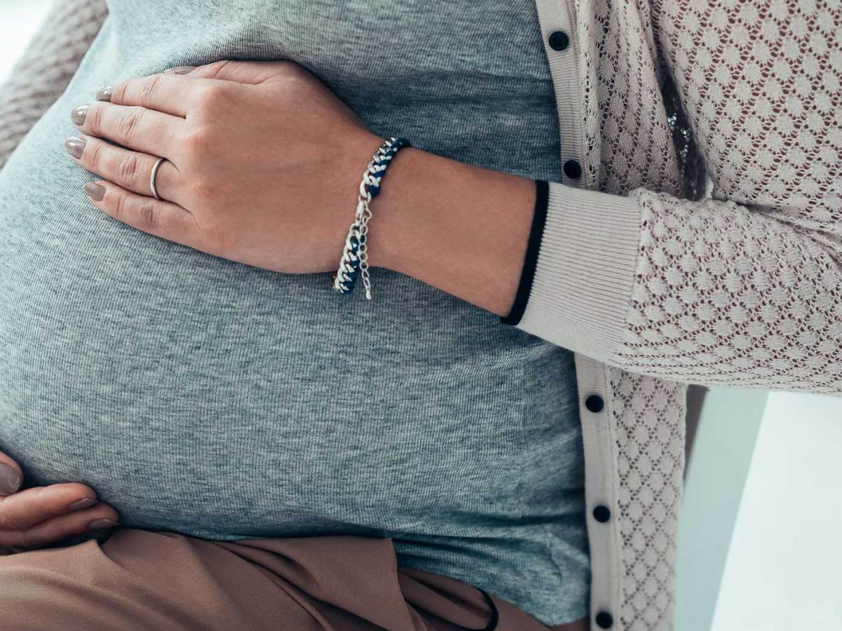 Nahaufnahme von Frauenh&auml;nden, die auf dem Schwangerschaftsbauch liegen.