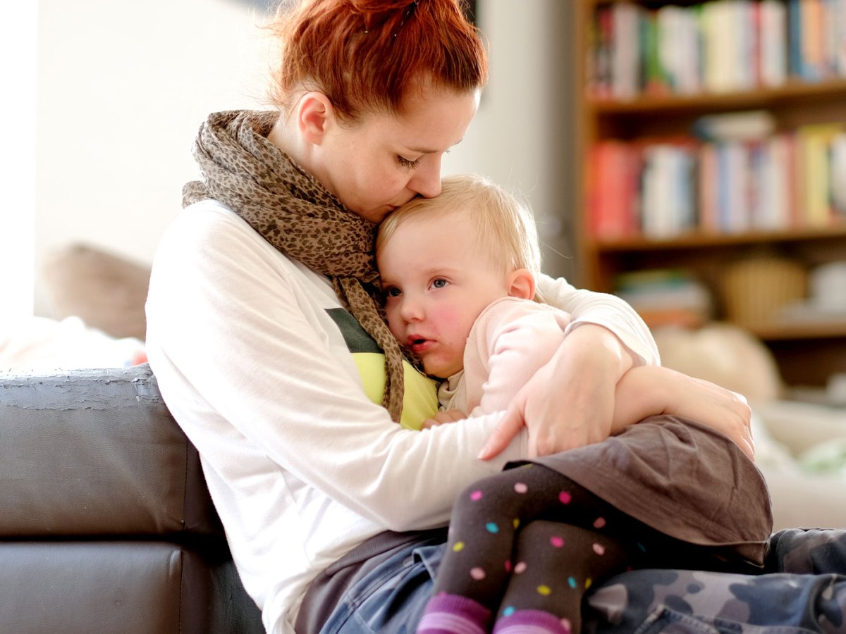 Erk&auml;ltete Tochter sitzt auf dem Scho&szlig; ihrer Mutter und beide kuscheln eine Runde.