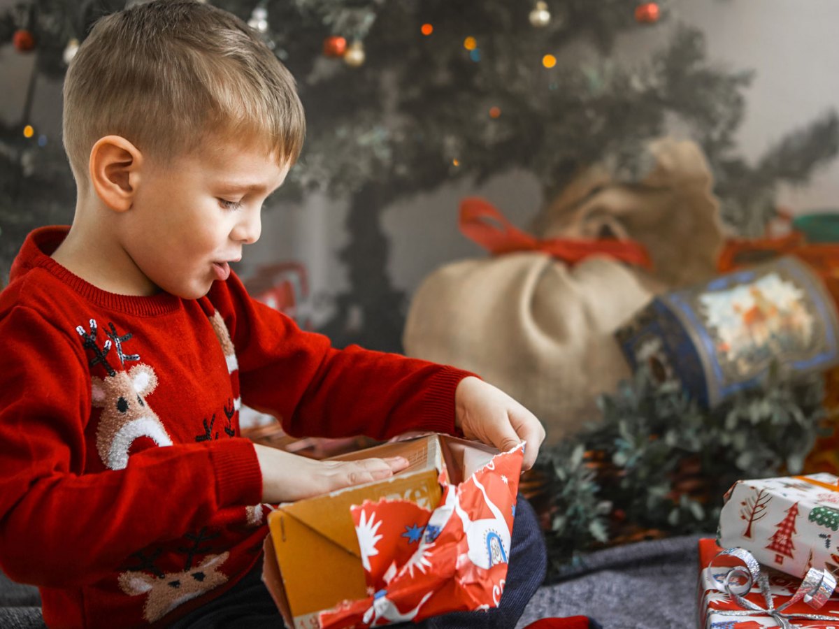 Junge, ca. 6 Jahre, packt aufgeregt ein Weihnachtsgeschenk aus.