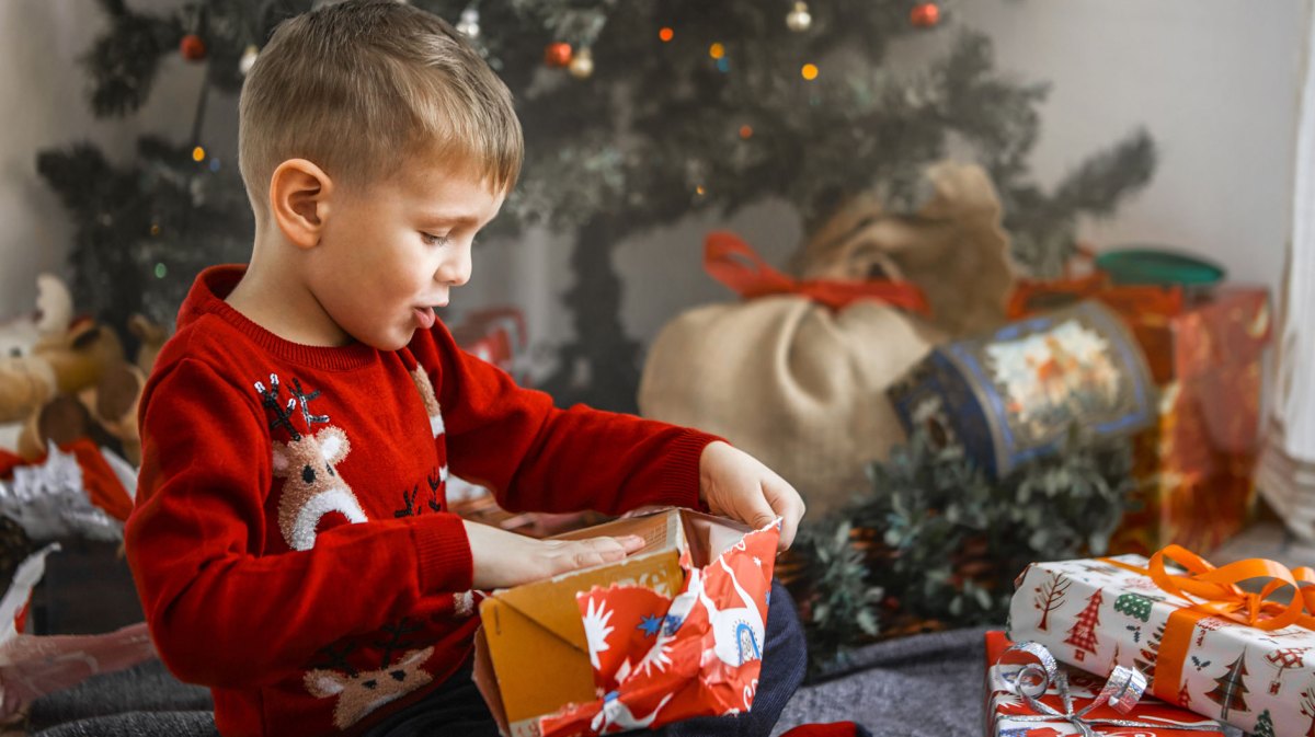 Junge, ca. 6 Jahre, packt aufgeregt ein Weihnachtsgeschenk aus.