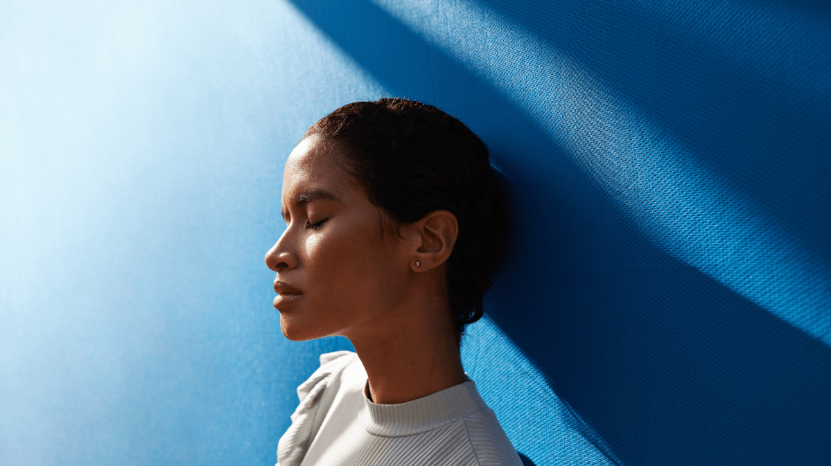 Frau vor einer blauen Wand blickt traurig