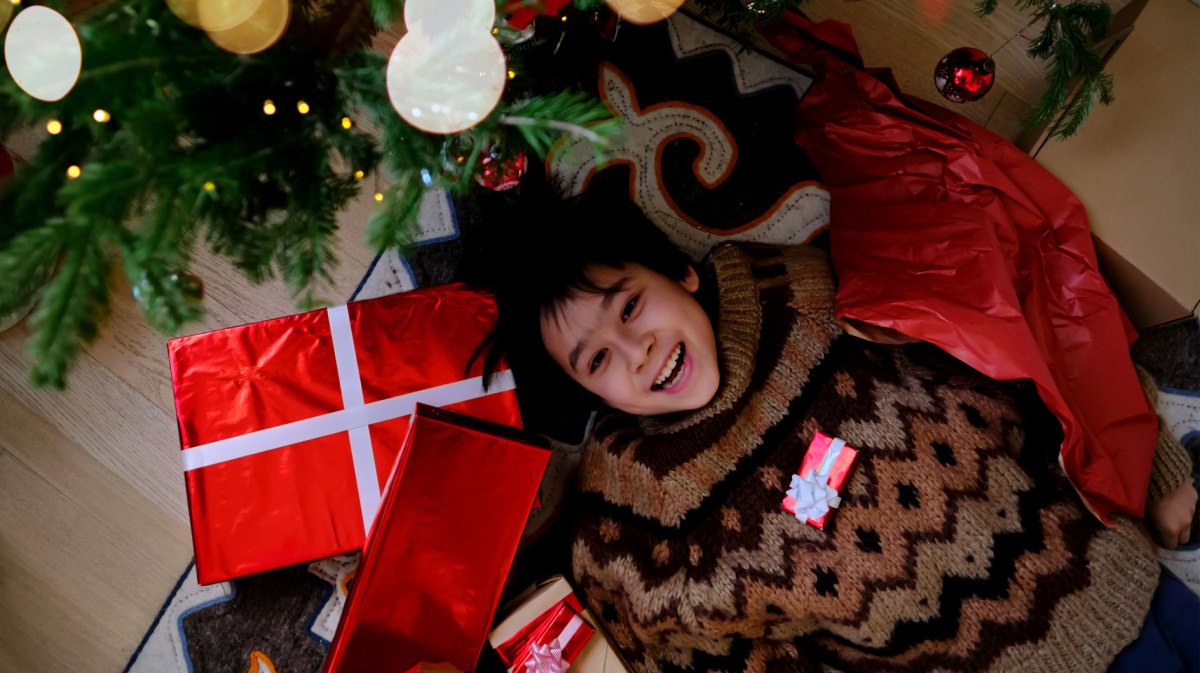 Junge im Teenageralter liegt auf dem Boden neben dem Weihnachtsbaum, umgeben von Weihnachtsgeschenken.