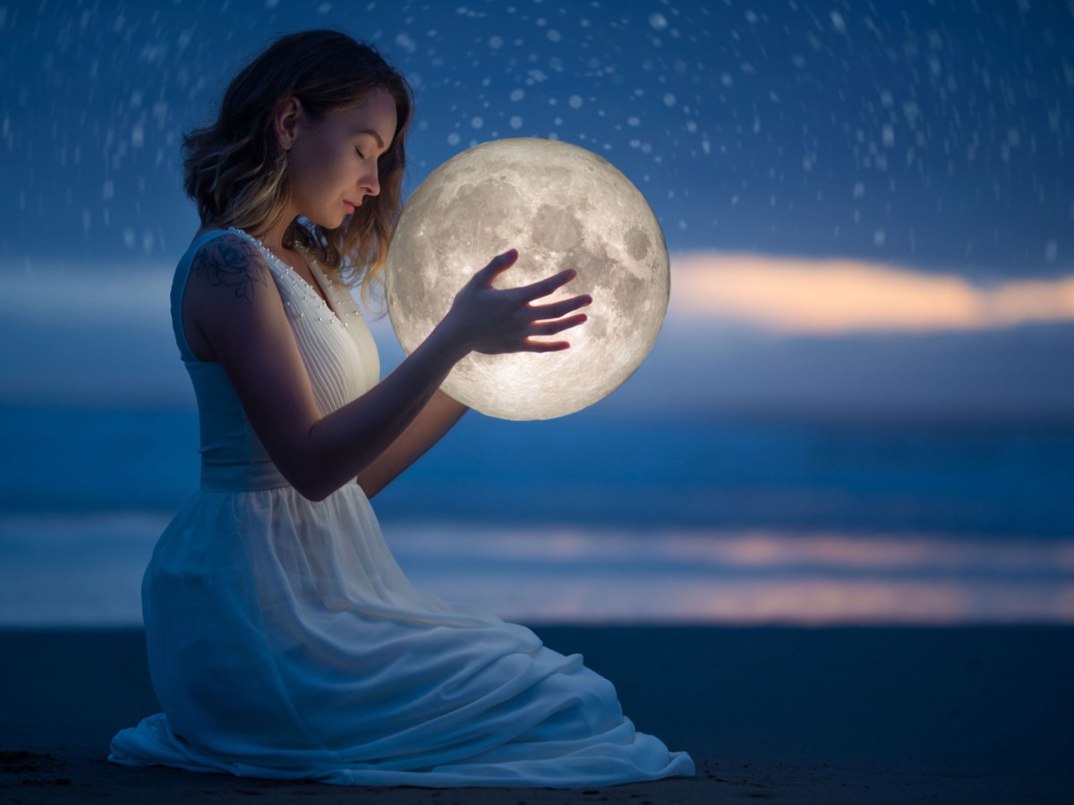 Frau im wei&szlig;en Kleid bei D&auml;mmerung am Strand h&auml;lt Mond in der Hand