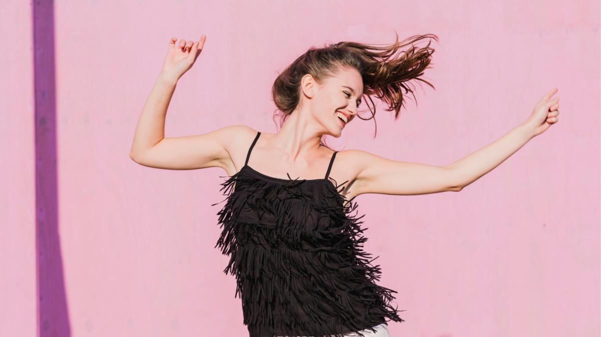 Frau mit schwarzem Top tanzt vor einer pinken Wand.