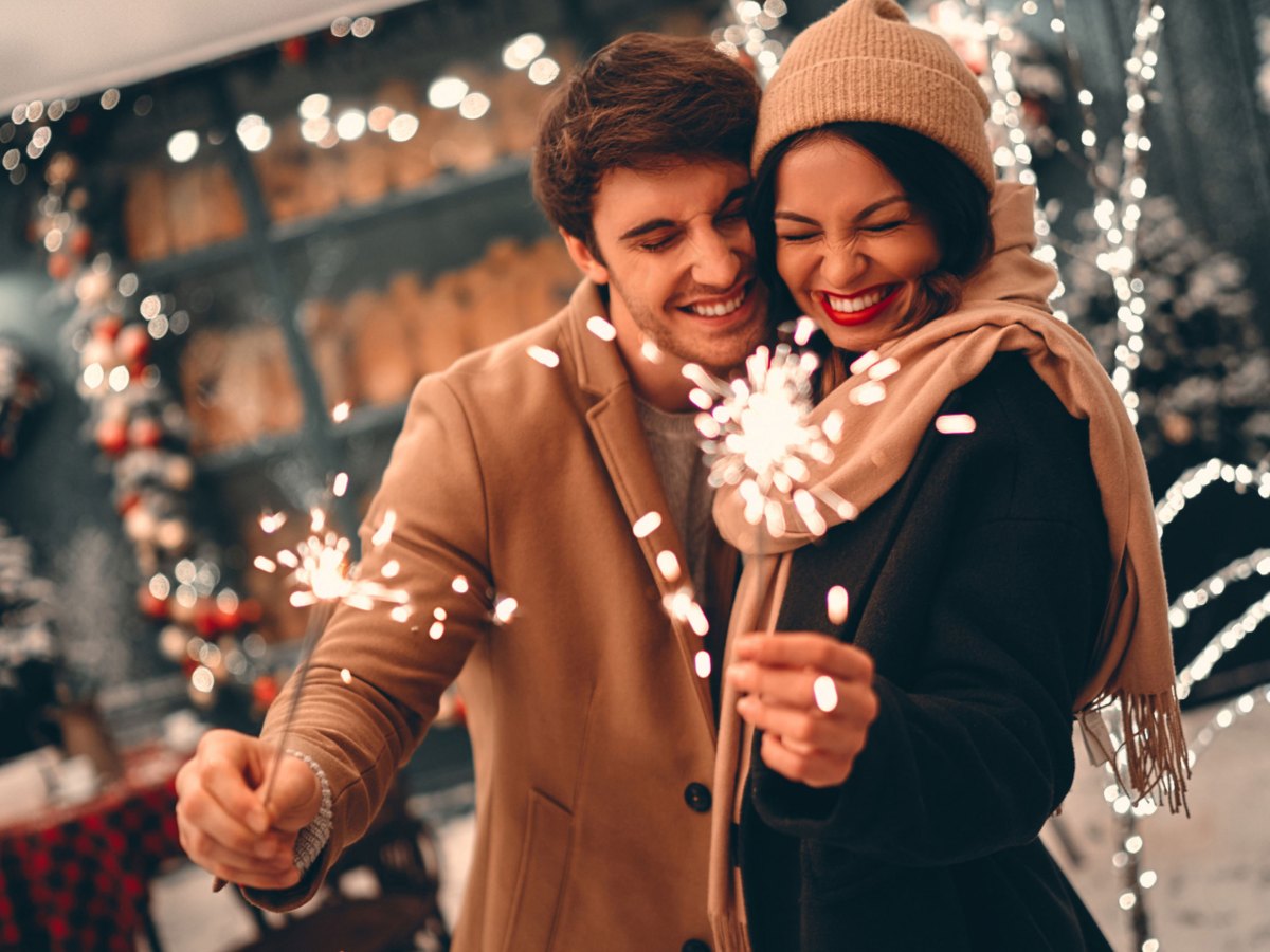 Mann und Frau in Winterbekleidung vor weihnachtlich geschm&uuml;cktem Haus, mit Wunderkerzen in der Hand.
