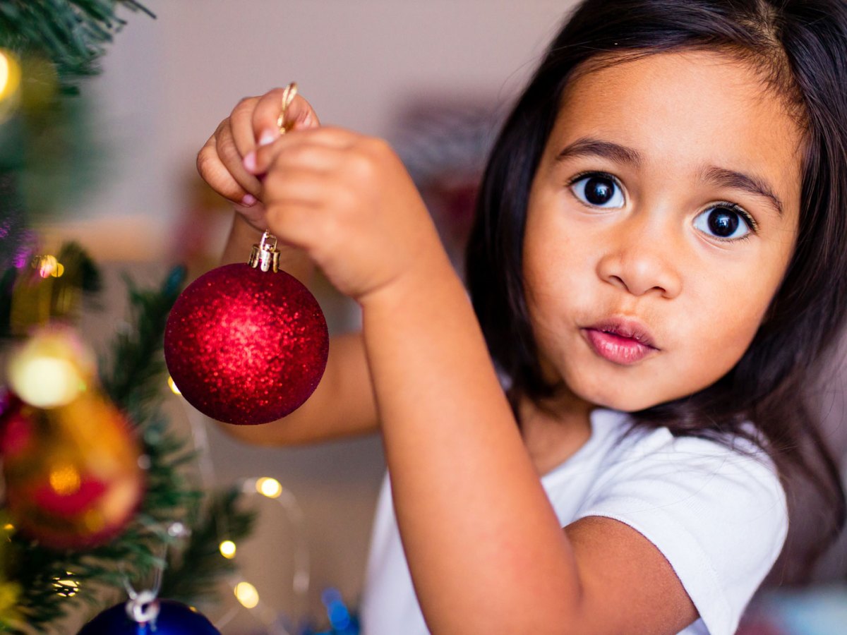 Nahaufnahme eines kleinen M&auml;dchens, ca. 6 Jahre alt, das den Weihnachtsbaum mit Kugeln schm&uuml;ckt.