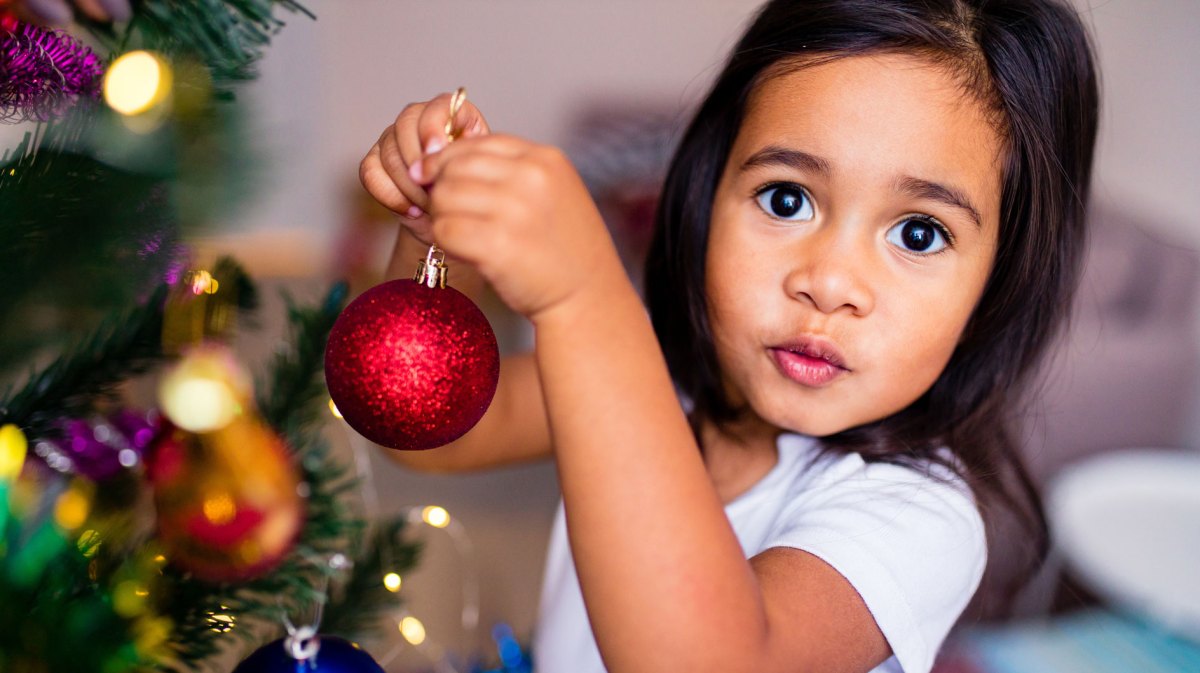 Nahaufnahme eines kleinen Mädchens, ca. 6 Jahre alt, das den Weihnachtsbaum mit Kugeln schmückt.