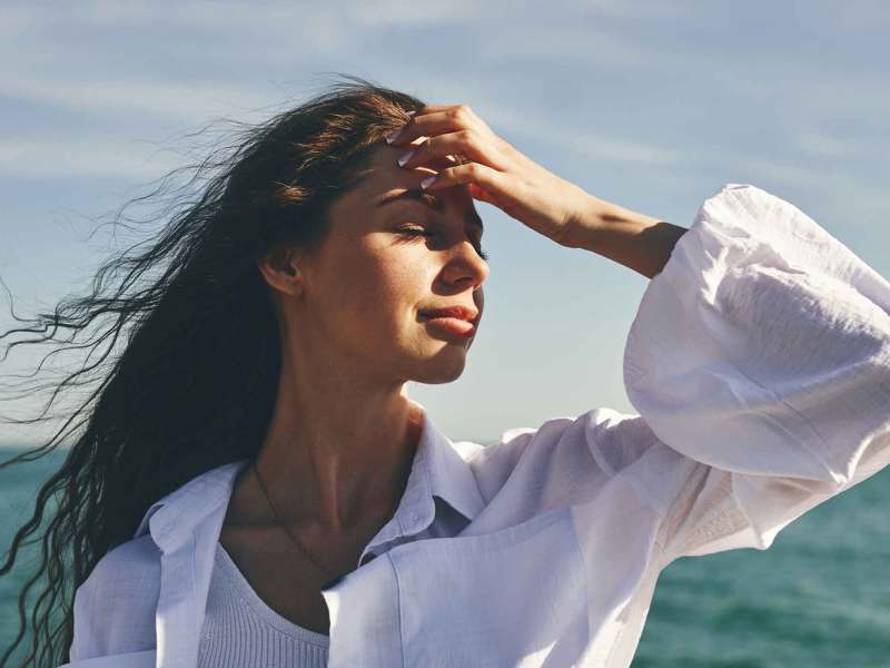 Junge Frau mit langen dunklen Haaren steht am Meer.