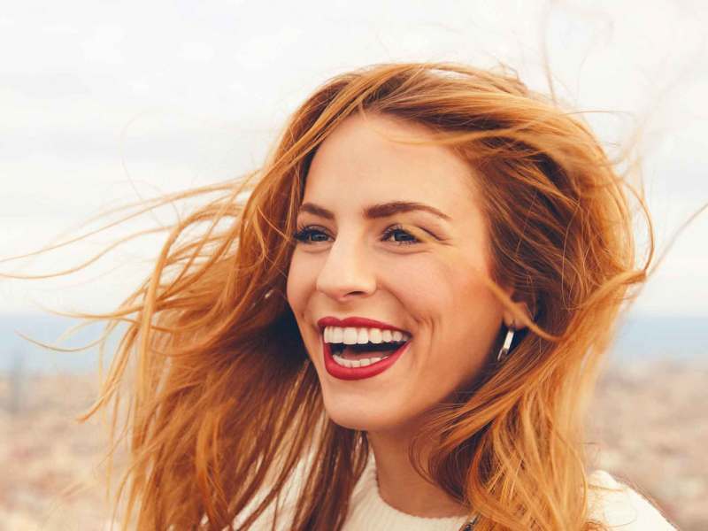 Lachende junge Frau steht draußen und lacht laut.